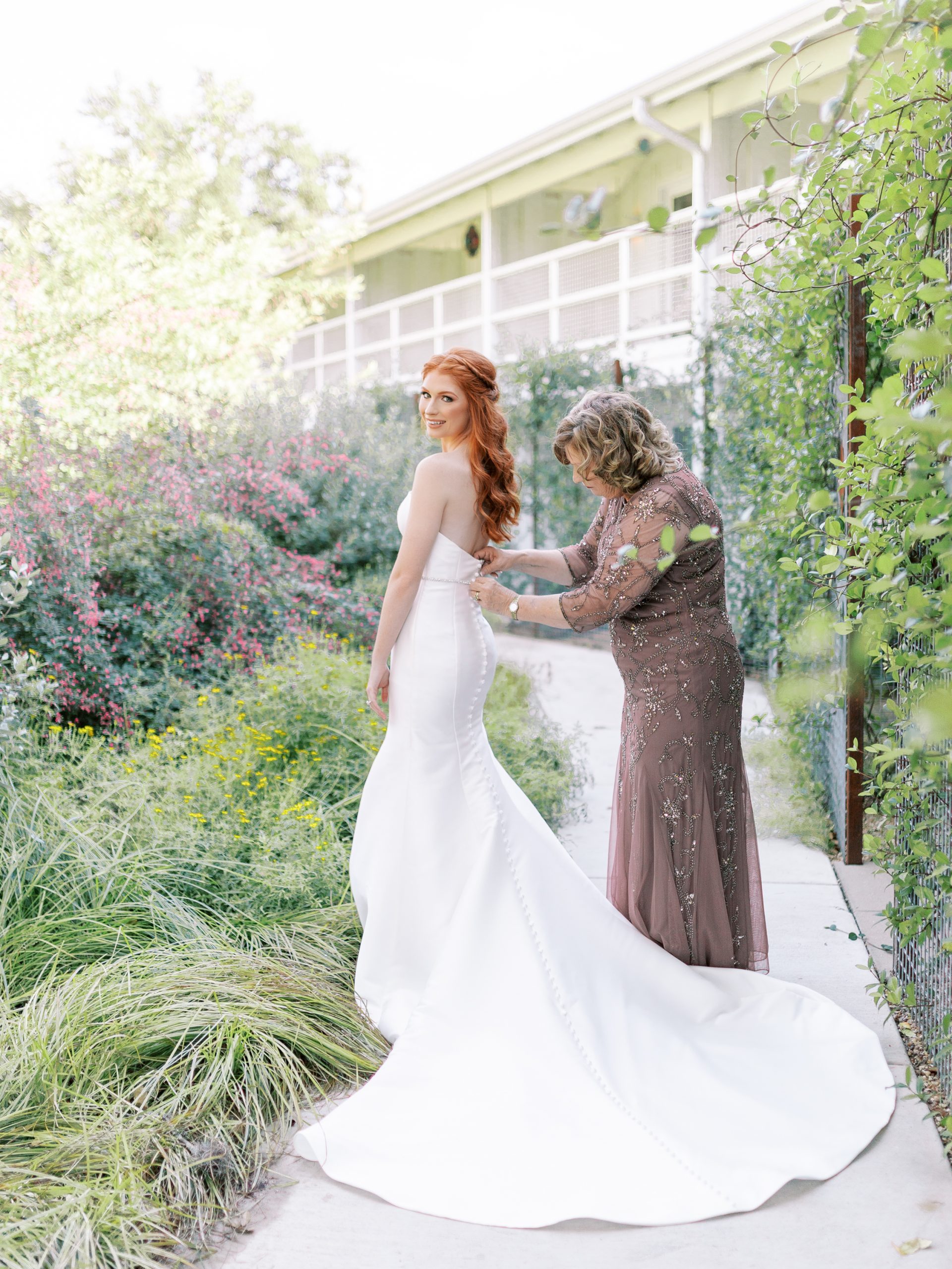 mom and bride putting on the bride's dress in garden